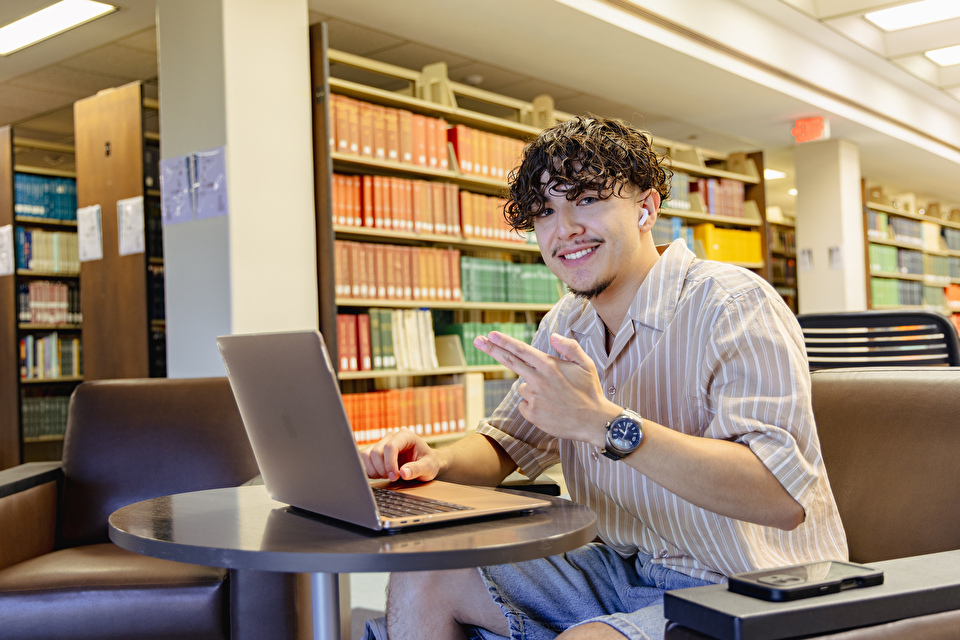 A student holds up an "Axe em" hand sign while studying in the library
