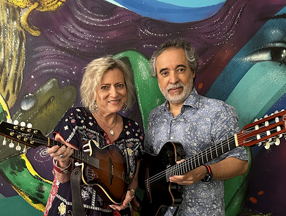 Photo of Juan Carlos Ureña and Jeana Paul Ureña holding guitars in front of a colorful backdrop