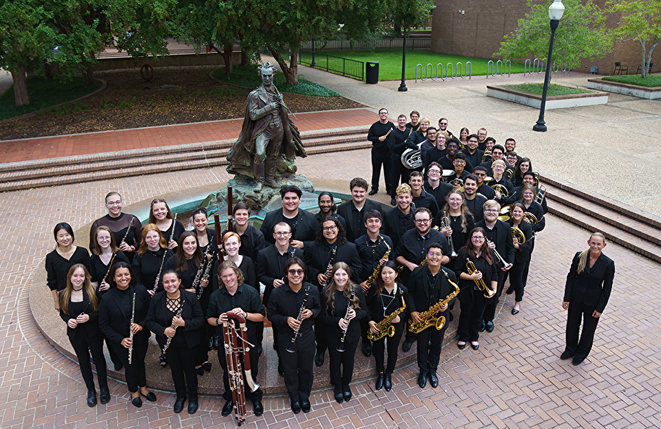 Wind ensemble photographed outdoors around Stephen F. Austin statue/fountain.