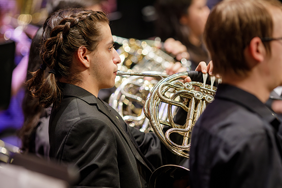 Photo of French horn player performing among fellow musicians