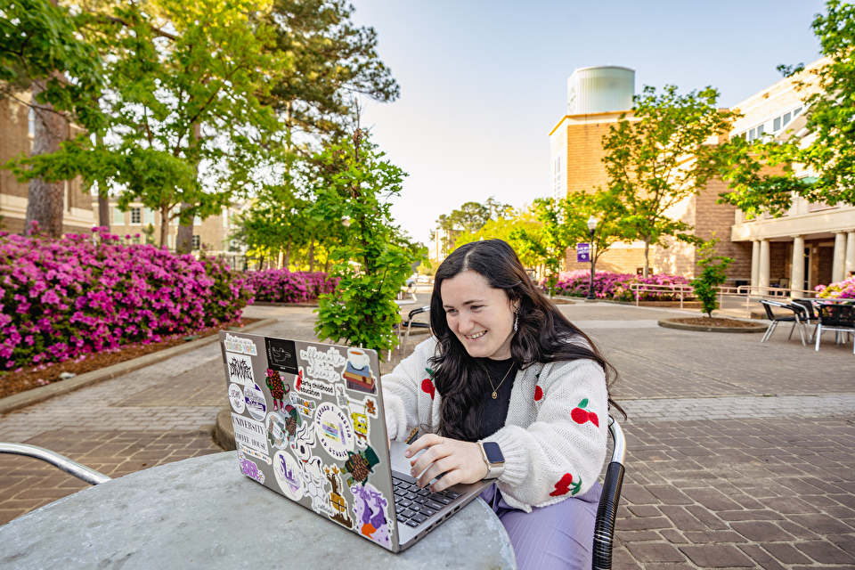 A students works on a laptop outside on campus