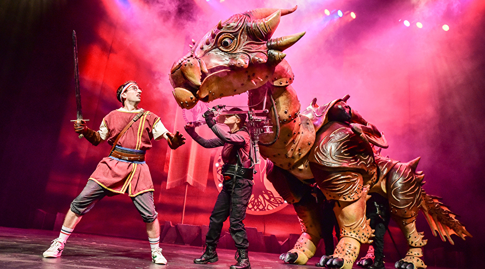 Photo of a character with sword battling a giant mythical dragon puppet on a stage