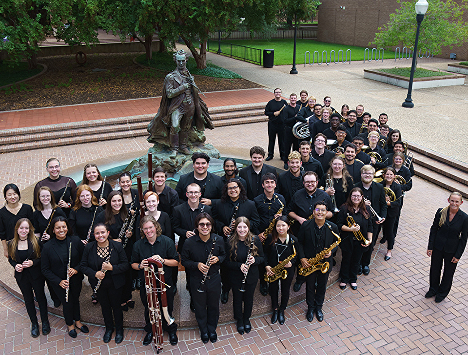 Photo of the Wind Ensemble and Dr. Tamey Anglley posed around the statue of “Surfin’ Steve”